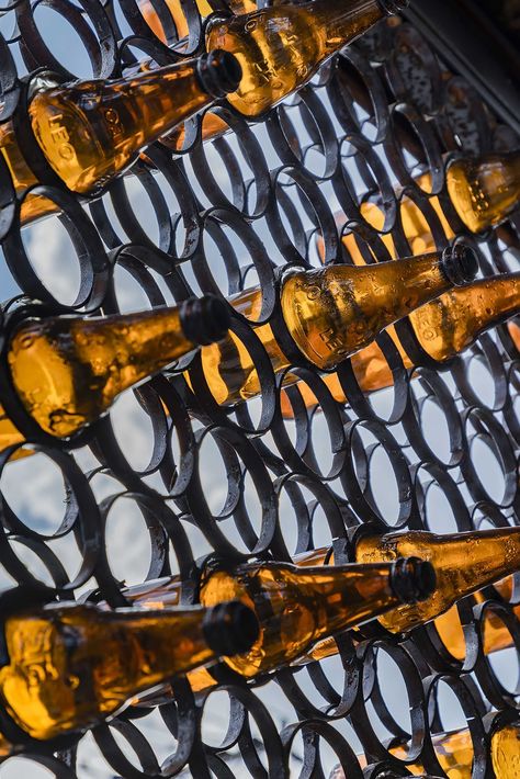 A modern cafe with a facade that features metal rings that hold recycled beer bottles. Wood Banquette, Terrazzo Counter, Brick Tile Floor, Recycled Beer Bottles, Recycle Metal, Small Seating Area, Glass Facade, Big Families, Hidden Lighting