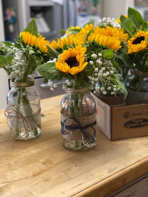 Sunflower centerpieces for our daughter’s graduation party. Mason jars from Walmart, sunflowers and baby’s breath from local grocery store, and ribbons and twine from Michael’s. I used double-side tape to attach the wide ribbon to the jars then tied the smaller ribbon around that. Add about 2-3 inches of water and you’re done. Sunflower Mason Jar Centerpieces, June Wedding Colors, Fairy Lights Wedding, Sunflower Centerpieces, Sunflower Vase, Party Table Centerpieces, Hanging Mason Jars, Western Party, Wide Mouth Mason Jars