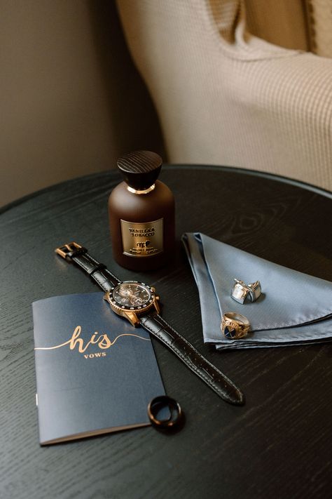 a grooms vows, watch, vanilla+tobacco cologne, wedding band and cufflinks sit on a dark wood table side a blue-grey pocket square. Wedding Details Photography Groom, Men’s Getting Ready Wedding, Western Wedding Flatlay, Groom Details Photography, Groom Flatlay, Groom Detail Shots, Wedding Band Tattoos, Grooms Details, Wedding Accessories Photography