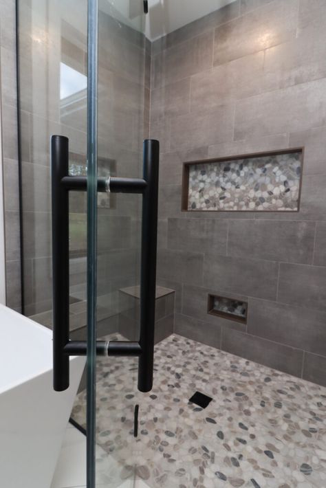 Gray tile shower with light pebble flooring. Glass shower door with black accents. Shower Tile Remodel Ideas, Bathroom Shower Tiles Gray, Gray Tile Master Bath, Gray Tiled Bathrooms Ideas, Grey Tile Shower Ideas Master Bath, Large Gray Tile Shower Ideas, Grey And Black Shower Tile Ideas, Bathrooms With Gray Tile, Black And Grey Shower Tile