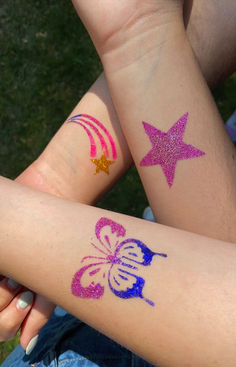 this pin shows three glitter tattoos on a group of peoples' arms. One tattoo is a pink star, one is a blue and pink butterfly, the last is a shooting star with a gold star and pink ombre lines. Glitter Tattoo Temporary, Glitter Tattoo Designs, Diy Glitter Tattoos, Glitter Tattoo Summer, Glitter Temporary Tattoos, Temporary Glitter Tattoo, Glitter Tattoo Aesthetic, Glitter Tattoo Permanent, Glitter Bar Ideas