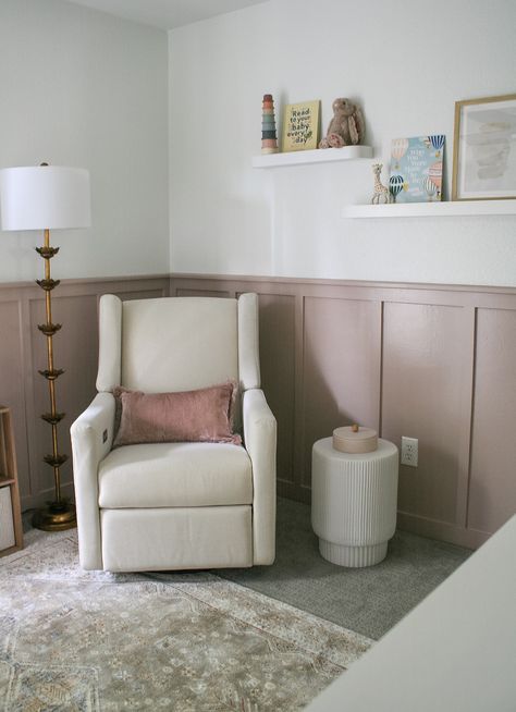 Nursery glider and side table in a small room. Cute organization of floating shelves on the walls, side table next to the glider, and cube storages for books and toys. White walls with pink board and batten. Nursery Wall Board And Batten, Small Nursery Ideas Panelling, Nursery With Built In Bookshelves, Panelling Walls Nursery, Baton Board Wall Nursery, Dado Rail Nursery Pink, Pink Wall Panelling Nursery, Pink Wainscoting Nursery, Light Pink Board And Batten