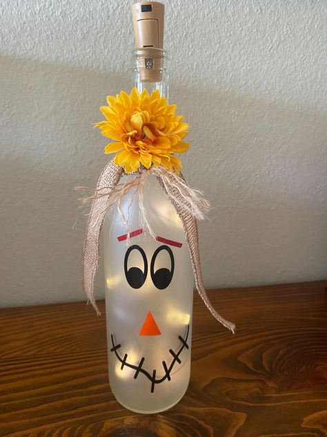 Light up your fall decor with a whimsical scarecrow lighted wine bottle.  The frosted bottle features an adorable scarecrow face glowing warmly with LED lights inside.  Perfect for a rustic touch to you fall celebrations.  Makes a cute centerpiece or a thoughtful gift for your favorite fall enthusiast. Halloween Wine Bottles Diy, Halloween Wine Bottle Crafts, Halloween Wine Bottles, Face Glowing, Scarecrow Face, Bottles Diy, Wine Glass Designs, Painted Bottles, Hand Painted Bottles