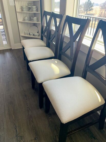 It’s DIY time again, and this time I’m sharing how I gave my dining area an easy and inexpensive makeover with this simple Chair Cover DIY using painter’s drop cloth.And by simple, I mean really simple. Can you operate a staple gun? Then you can completely recover your chairs in an hour or two, depending on how many chairs you have.BEFORE my Chair Cover DIYHere’s my “before” picture… I love our dining table because it’s big and can seat a lot of people. Here it is with 8 chairs, but… How To Make Dining Chair Seat Covers, Recover Dining Chair Seats, Reupholster Chair Dining Seat Cushions, Cover Chairs With Fabric Diy, How To Cover Chairs With Fabric, How To Recover Dining Room Chairs, Upholstering Dining Chairs Diy, Diy Dining Chairs Makeover, Diy Reupholster Chair