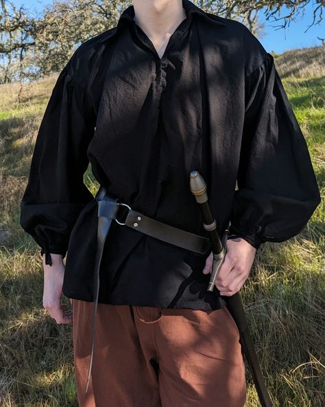 This medieval pirate shirt is the perfect piece for the full adventurer's look! Made with premium fine cotton, this shirt is super lightweight and breathable, making it easy to wear, no matter the weather. Made with big sleeves and a comfortable collar, no matter how you move in the shirt, whether that is fighting off bandits, receiving an award from a damsel, or scaling the Cliffs of Insanity, this shirt will move with you. The interior seams of the shirt are hemmed to prevent fray and the sleeves are fastened with ties around the wrists for an adjustable fit. - 100% premium durable cotton - Lightweight and easy to wear - Black and white colors - Handmade on the central coast of California, USA *Model is 6'3", and is wearing a size M* Medieval Clothing Men, Medieval Pirate, Pirate Shirt, Poet Shirt, Medieval Clothes, Blouse Man, Big Sleeves, Pirate Shirts, Black Costume