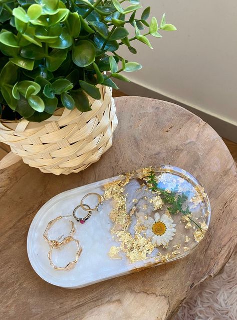 Tray tray made of crystal epoxy resin. This pretty cup can be used to put your jewelry, your keys, your perfumes, your make-up, your glasses, and will match in each room of your house ✨ If you are an artist or nail artist, you can use this decorative tray in flowers to affix your colors, varnishes or brushes. Each tray is encrusted with a dried daisy, plants and gold leaf. The pearly white dye used is natural. Each piece is unique, handmade with 💜 in our workshop in France. 📲 Do not hesitate t Pretty Cups, Vide Poche, Diy Resin Art, Jewelry Tray, Trinket Tray, White Jewelry, Flower Lover, Resin Diy, Decorative Storage