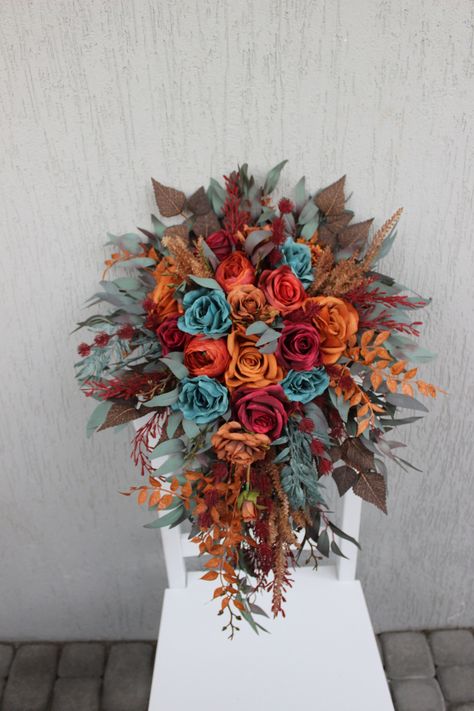 This cascading fall wedding bouquet is a captivating masterpiece, featuring a rich and moody color scheme that marries dark teal, rust, and burgundy flowers. The bouquet's lush design exudes a sense of opulence and warmth, making it an ideal choice for a fall wedding. The deep, luxurious hues of dark teal, rust, and burgundy come together to create a truly dramatic and stunning arrangement, adding a touch of elegance to the autumn celebration. ○ Color: teal, burgundy, rust, brown, green ○ Person Rust Teal Burgundy Wedding, Teal Burnt Orange And Burgundy Wedding, Spring Teal Wedding, Rust Burgundy Wedding, May Wedding Bouquet, Teal And Rust Wedding, Teal And Burgundy Wedding, Dark Teal And Rust Orange Wedding, Jewel Tone Fall Wedding