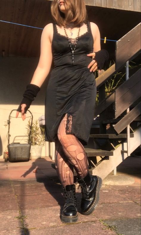 A mid-size person/girl wearing a black thrifted lace grandma vintage lingerie  dress, a black wide leather trench coat over it, ripped tights, black platform dr. Martens and multiple crystal rings and bracelets. 	The person is also wearing multiple silver necklaces, one in form of a moon and another in form of a fairy  necklace, a black rosary-style  bead necklace, a rose quartz crystal necklace and a black lace choker. Goth Tights Aesthetic, Moon Goth Outfits, Spring Outfits Goth, Summer Goth Clothes, Earth Tone Outfits Plus Size, Midsize Black Dress, Goth Slip Dress Outfit, Goth Midsize Outfits, Vampire Summer Outfits