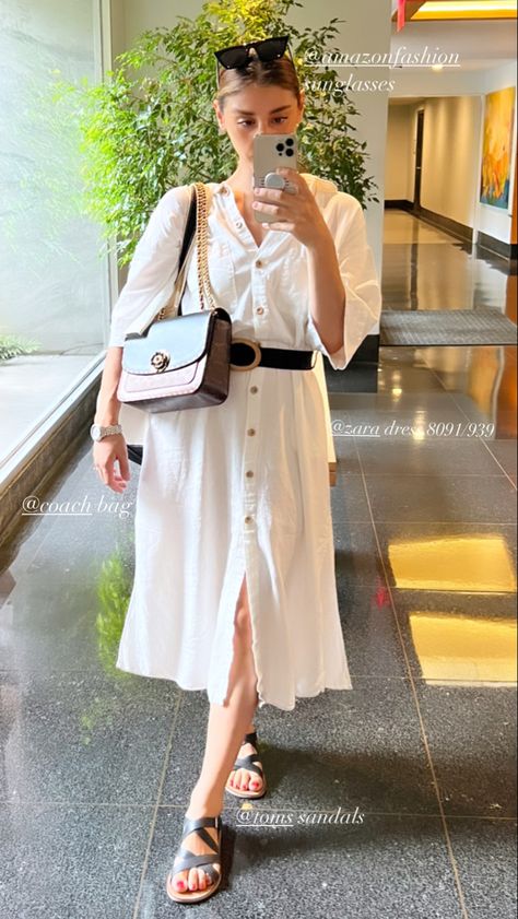 She is wearing a white dress with a black belt. She is holding a crossbody bag. She is wearing black and brown sandals. Zara Dress 2022 Summer, Dress 2022, Outfit Zara, White Summer Dress, Zara Dress, White Dress Summer, White Summer, Summer 2022, Zara Dresses