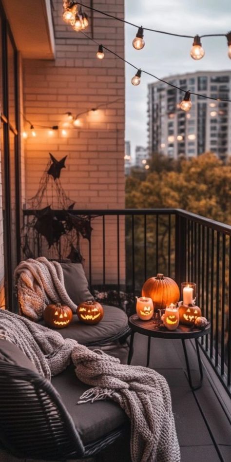 Cozy balcony decorated for Halloween with string lights, carved pumpkins, and blankets. Fall Decorations Apartment Small Spaces, Balcony Autumn Decor, Apartment Balcony Fall Decor, Apartment Decorating Halloween, Halloween Apartment Patio Decor, Fall Apartment Patio Decor, Apartment Balcony Decor Ideas, Halloween Apartment Decor Balcony, Apartment Porch Halloween Decorations