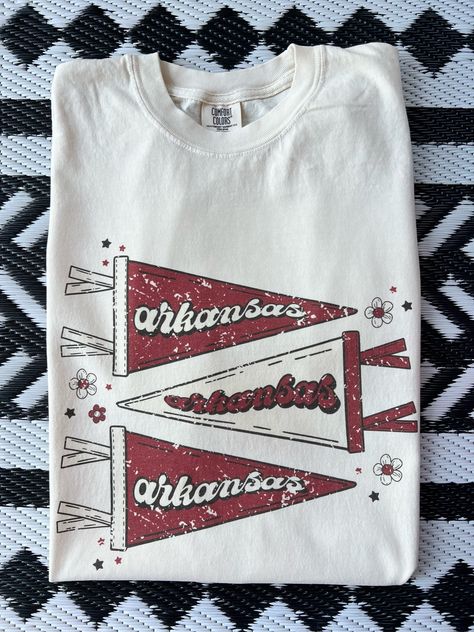 New product- Vintage Arkansas Pennant Shirt! Get ready to show off pride with our Vintage Pennant Shirt, a must-have for all fans! This unique design combines a vintage style with the fierce spirit of fans, creating a shirt that stands out from the crowd. Each shirt is meticulously printed by me using high-quality materials on a Comfort Colors shirt, known for its exceptional comfort and durability.  Available in sizes S to 3X, we've got you covered regardless of your preferred fit. The shirt features a classic crew neck and short sleeves, making it suitable for year-round wear. The flattering silhouette ensures a comfortable and stylish fit for both men and women. This design is an ideal choice for game days, tailgating parties, alumni events, or simply strolling around campus. Note: As e College Tee Shirts, Highschool Sports Shirts, Game Day T Shirts, Retro Baseball Shirt, Game Day Tops, Sports Sweatshirt Designs, Cute College Shirts, High School T Shirt Designs, Alumni Tshirt Design Ideas