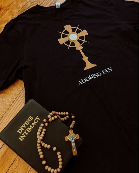 Y'all know I'm all for Catholic humor and this shirt was born of that adoration for humor and puns (there I go again...) Introducing "Adoring Fan" - a simple and SUPER Catholic tee. Beneath the glorious monstrance are the words "ADORING FAN", which has two meanings: 1) The wearer adores Jesus in the Eucharist and 2) The wearer also thinks that adoration is pretty spectacular Available in black, this unisex shirt is great to wear to holy hour, gift to priests or new Catholics, or anyone el... Holy Hour, Catholic Humor, The Eucharist, Eucharist, Unisex Shirt, Puns, Jesus, Humor, Fan