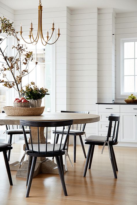 Black spindle chairs sit around a round brown dining table lit by a brass chandelier. Black Spindle Chairs, Spindle Chairs, Black Leather Dining Chairs, Brass Dining Table, Brown Dining Table, Black Chairs, Transitional Dining Room, Round Kitchen Table, Transitional Dining