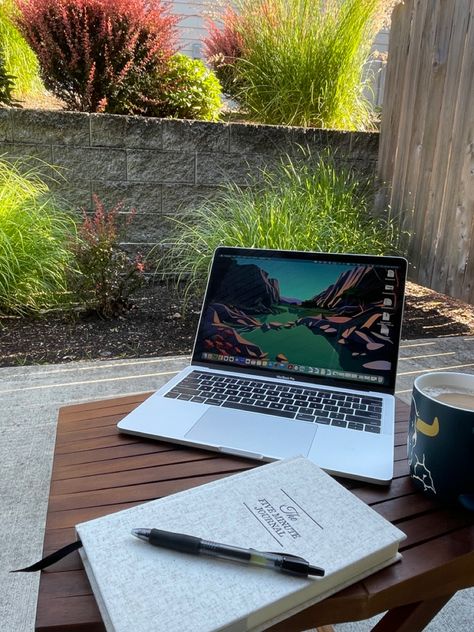 A laptop, mug of coffee, and a journal are sitting on an outdoor table on a patio. The patio is surrounded by bushes and plants. Outdoor Office Space Patio, Work At Home Aesthetic, Wfh Inspiration, Outdoor Office Space, Working From Home Aesthetic, Wfh Aesthetic, Work From Home Desk Setup, Home Desk Setup, Wfh Space