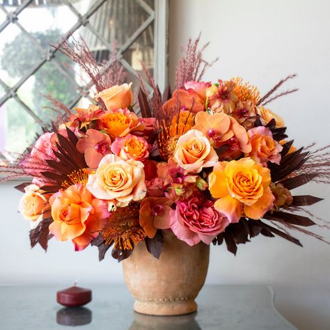 This stunning floral arrangement is sure to infuse your home with warmth and comfort. An enchanting mix of orange and pink roses, phalaenopsis orchids, butterfly ranunculus, and pink garden roses are accented with dried brown palm leaves and pin cushions. Sitting in a 6 1/2in tall terracotta pot, "Dawn To Dusk" is the perfect addition to any home. Halloween Bunco, Hotel Flower Arrangements, Thanksgiving Floral Arrangements, Pink Thanksgiving, Fall Floral Centerpieces, Butterfly Ranunculus, Pumpkin Floral Arrangements, Hotel Flowers, Thanksgiving Floral