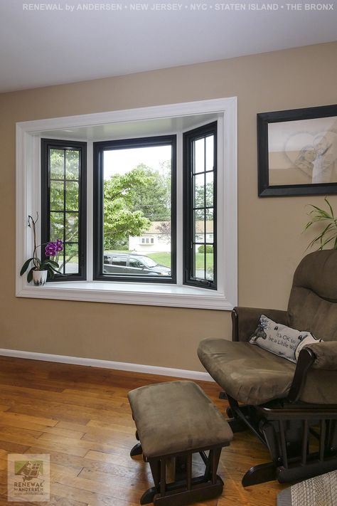 Beautiful new bay window, with white frame and black windows, that we installed in this charming sitting area. This bay window is made up of three windows, a large picture window in the middle and two smaller casement windows with grilles on either side. Find out more about getting new windows in your home from Renewal by Andersen of New Jersey, New York City, Staten Island and The Bronx. Painted Bay Windows Interior, Picture Window Replacement Ideas, Bay Window Replacement Ideas, Modern Bay Window Exterior, Black Bay Window, Window Replacement Ideas, Picture Window Ideas, Bay Window Exterior Ideas, Picture Windows Exterior