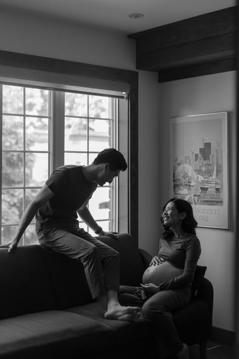 A woman sits on the couch, holding her belly, she looks up at her partner who is sitting on the back of the couch, He smiles down at her. Maternity Shoot In Living Room, Documentary Photography Maternity, Indoors Maternity Shoot, Maternity Photography Documentary, Documentary Maternity Shoot, In Home Maternity Photography, Chic Maternity Shoot, Casual At Home Maternity Photos, In House Maternity Shoot