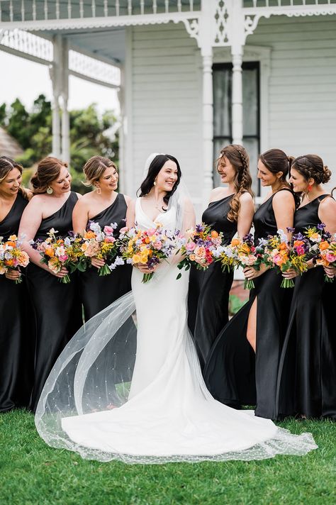 Bride with bridesmaids in black gowns with colorful bouquets Black And White Weddings With A Pop Of Color, Black Bridesmaid Wedding Party, Black Bridesmaid Dresses Colorful Shoes, Summer Wedding Colors With Black, Black Wedding With Bright Flowers, Black With Bright Colors Wedding, White Wedding Bouquets With Pop Of Color, Black And White Wedding With Colored Flowers, Black Bridesmaid Dresses Spring Wedding