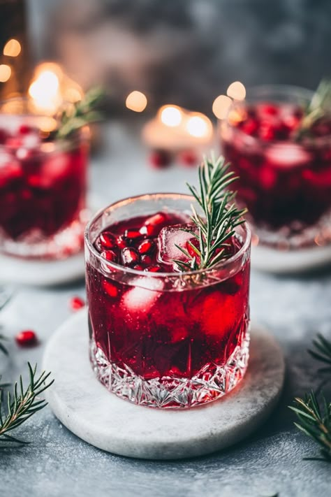 Three glasses of red cocktails garnished with rosemary sprigs on a marble surface, with lights in the background. Pomegranate Drinks Non Alcoholic, Pomegranate Drink Recipes, Persian Drinks, Evening Food Ideas, Pomegranate Recipes Drinks, Pomegranate Photography, Weihnachtlicher Cocktail, Pomegranate Drink, Ginger Cocktail Recipes