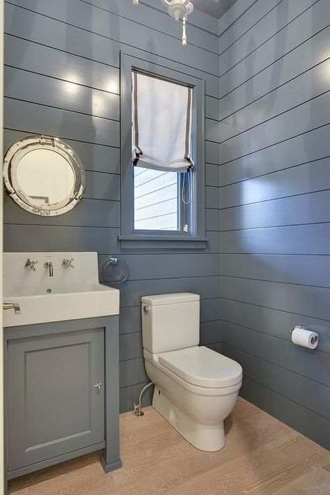 Blue cottage powder room boasts blond oak wood floors framed by blue shiplap walls and is fitted with a white porcelain toilet positioned beneath a window dressed in a gray grosgrain roman shade. Window Above Toilet, Shiplap Powder Room, Cottage Powder Room, Toilet Design Ideas, Blue Shiplap, Shiplap Bathroom Wall, Blue Walls Living Room, Vertical Shiplap, Above Toilet