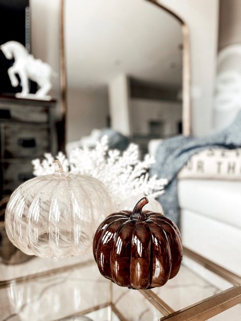 Two glass pumpkins and a glass pumpkin candle sit on a gold and glass coffee table next to a faux coral decor object. Beige Fall Decor, Autumn Apartment, Glass Pumpkin Decor, Coastal Fall Decor Ideas, Target Glass, Fall Apartment, Apartment Therapy Inspired Decor, Glass Decor Ideas, Fall Coffee Table Decor