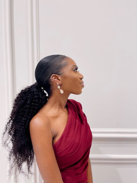 A girl in a sleek low, kinky curly ponytail and burgundy one shoulder dress stands facing her left, showing off her hair Ponytails For Weddings Bridesmaid, Black Women Slick Back Ponytail, Bridal Ponytail Black Women, Slicked Back Prom Hairstyles, Black Women Bridal Party, 4c Ponytail Hairstyles Extension, Bridal Ponytail Hairstyles Black Women, Low Ponytail Curly Hair, Low Ponytail Natural Hair