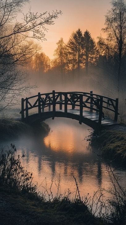 In the early hours of the morning, a wooden bridge casts a delicate silhouette over a quietly flowing river. The mist, suffused with the warm glow of sunrise, creates an ethereal atmosphere that softens the landscape. Surrounding trees, partially obscured by the fog, add a sense of mystery and depth to the tranquil scene, inviting a moment of peaceful reflection. Morning Flow, Fog Photography, Sunrise Images, Beach Silhouette, Flowing River, Misty Morning, Wooden Bridge, Stone Bridge, Quaint Village