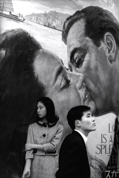 Henri Cartier-Bresson photo of a man and woman standing juxtaposed against a painted background of a couple kissing. Photography juxtaposition examples. Robert Frank, Robert Doisneau, Henri Cartier Bresson, Famous Photographers, French Photographers, Foto Vintage, Magnum Photos, Great Photographers, Foto Art