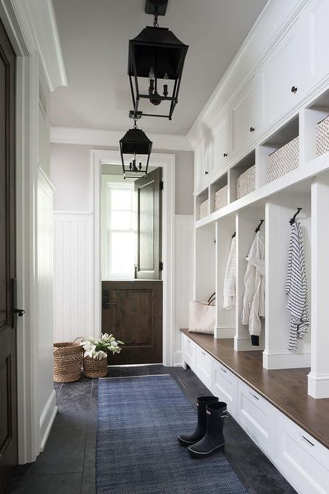 A walnut dutch door flanked by a vertical beadboard trim opens to a blue runner lit by two carriage lanterns hung in front of a white storage bench accented with a wood top fixed beneath open lockers. Vstupná Hala, Farmhouse Mudroom, Mud Room Entry, Mudroom Decor, Mudroom Design, Foyer Decorating, Dutch Door, غرفة ملابس, Hus Inspiration