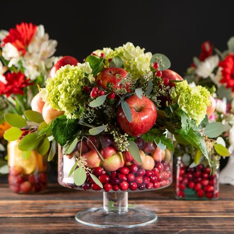 It’s always nice to have a floral arrangement displayed on the table to enjoy the colors of the season, but why not add a little extra flair with a dash of seasonal produce? We put together a few ideas of how to incorporate this season’s produce in a beautiful centerpiece. Fruit Basket Centerpiece Ideas, Floral Arrangement With Vegetables, Fruit Flower Centerpiece, Pomegranate Floral Arrangement, Floral Arrangements With Fruit, Produce Centerpieces, Apple Centerpiece Ideas, Fruit Centerpiece Ideas, Fruit And Flower Arrangements