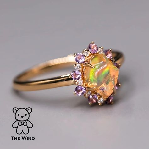 Hey everyone! Today, let me introduce the Mexican Fire Opal Amethyst Diamond Engagement Halo Ring in 18K Yellow Gold. Designed by our artist for someone truly special, this unique ring features a circle of amethyst embracing the Mexican Fire Opal. Ideal for engagements and anniversaries, its uniqueness ensures you won't find a match. Express your love uniquely! 💖 #EngagementRing #uniquelove #OpalJewelry #OpalLove #DiamondRing #FineJewelry #JewelryLove #Ring #JewelryMagic #DiamondHalo #LuxuryF... Opal And Gold Ring, Opal And Diamond Wedding Ring, Amethyst And Opal Engagement Ring, Fire Opal Wedding Ring, Opal Sapphire Ring, Whimsy Rings, Gold Opal Rings, Rarest Gemstones, Fire Opal Engagement Ring