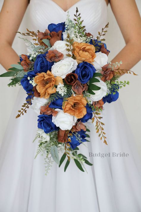 This lovely assortment of royal blue, brown and white roses is bound to turn heads on your wedding day. This lovely cascading brides’ bouquet from the is an absolutely breathtaking arrangement for any bride to be, in any season. Bright greenery and light brown magnolias complete the look and add a delicate realism to this beautiful bouquet. This bouquet is 10” wide, 18” long, and is crafted by our in-house florists without using a foam base to anchor the flowers to the bouquet. Instead, we wire Blue And Brown Bouquet, Royal Blue Boho Wedding, Royal Blue Country Wedding, Royal Blue Fall Wedding, Royal Blue And Orange Wedding, Blue Arrangements, Royal Blue Wedding Decorations, Blue Fall Wedding, Zion Wedding