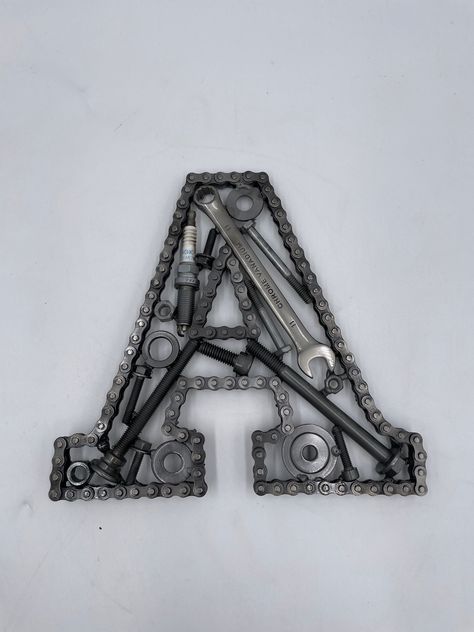 Car Parts Initial Letter A, Monogram Letter Wall Art, Automotive Wall Decor Here you can order a custom built letter 'A' created with automotive parts. Timing chain outlines the letter, with a great variety of car parts used in the design. This is a handmade - built to order item, so if you would like any particular brand of car parts included in the build, please let me know! You can order your letter to be 8, 11 or 16 inches in height. The letters can be built at any size, so if you would pref Diy Car Parts Decor Ideas, Car Part Art Automotive Decor, Horseshoe Welding Projects Beginner, Car Themed Decor, Easy Welding Projects To Sell, Welding Projects Decor, Things To Weld, Welding Shop Organization, Scrap Metal Art Car Parts