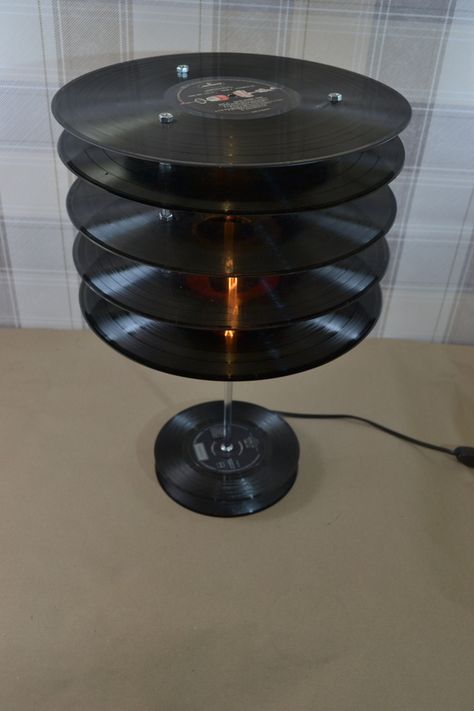 An upcycled stack of 12-inch vinyl records, handcrafted into a stylish funky and cool retro table lamp. The shade is completely unique, due to the characteristics of the individual records sourced. Overall this is a very classy looking item and well made. This Vintage Lamp is a real eye-catcher, perfect for an Art Deco and vintage-inspired style! Light is one of the most powerful décor tools at your disposal. From the natural light that streams in through your kitchen window to the soft ambient Antique Lamps Vintage Lighting, Film Lamp, Upcycle Lamp, Recycle Table, Huge Lamp, Funky Lamps, Art Deco Lamp, Deco Lamp, Book Lamp