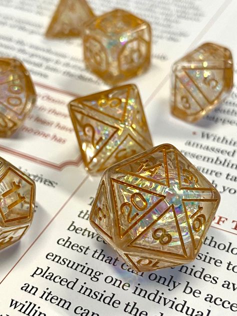 "Arcane Gate" -Brand new style! This full 7 piece dice set has delicate arcane patterns on each face, and the same popular and captivating prismatic look of many of the best selling sharp edge sets, in a rounded smooth resin finish. The iridescent foil shines through the translucent resin, making this set sparkle with inner fire from all angles. Now available in both gold and light blue tones!  Fun to roll, and balanced for gameplay.  Comes packaged in a small woven dice bag. Other color options D&d Gifts, Cute Dnd Dice, Gold Moodboard, Cool Dice, Cool Dnd Dice, Crystal Dice, Iridescent Foil, Resin Making, Dnd Dragons