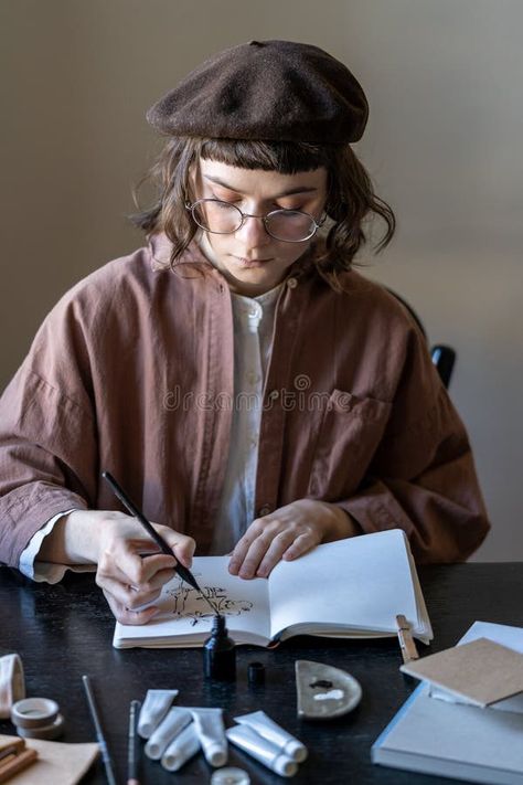 Young focused female artist wearing beret and glasses sitting at table painting with black ink stock photos Table Painting, Sitting At Table, Female Artist, Wearing Glasses, Painted Table, Female Artists, Stock Images, Stock Photos, How To Wear