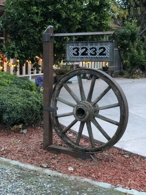 Wagon Wheel Address Sign Ideas, Wagon Wheel Garden Decor, Landscaping With Wagon Wheels, Wagon Wheel Display Ideas, Wagon Wheel In Garden, Farmhouse Wagon Wheel Decor, Ideas For Wagon Wheels, Wagon Wheel Address Sign, Wagon Wheel Mailbox Ideas