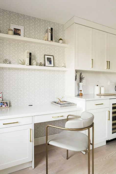 A separate office wasn’t in the works for the homeowners, but they found a solution: a kitchen desk niche. It’s just right off the main kitchen area and matches with the rest of the white cabinetry. Bold, patterned wallpaper gives the desk a sense of separation from the rest of the kitchen, too. Desk On Kitchen Counter, Home Office Near Kitchen, Home Office Off Kitchen, Kitchen Nook Office Ideas, Office Space In Kitchen Area, Kitchen Computer Desk, Kitchen Desk Built In, Office Desk In Kitchen, Built In Desk Area In Kitchen