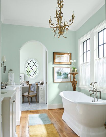 Airy bathroom with pastel green walls, chandelier, soaking tub, sink and cabinets, wall art, large windows, and a desk and chair. Mediterranean Color Palette, Mint Green Paints, Mint Paint, Bathroom Wall Colors, Light Green Walls, Mediterranean Living Room, Mission Style Homes, Mint Green Walls, Mint Walls