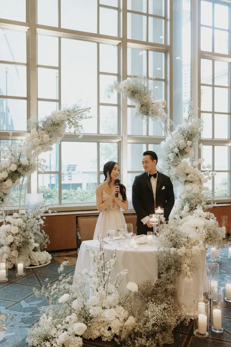 An elegant and modern head table surrounded by clouds of babies breath and white roses. A small sweetheart table with a ground floral arrangement at the base. Babies Breath Sweetheart Table, Small Sweetheart Table, Sweetheart Table Wedding Elegant, Modern Sweetheart Table, Wedding Bridal Table, Modern White Wedding, Tall Floral Arrangements, Bride Groom Table, White Floral Arrangements