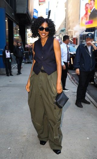 Actor-comedian Ayo Edebiri casually posing on a city street, smiling at the camera. She is dressed in the fashion brand Loewe, and has livened up the ultra-popular suit vest top by leaning into the masculine; pairing it with a pair of olive green barrel trousers outfitted with utilitarian hardware, oversized sunglasses, and square-toed boots. Ayo Edebiri, Victoria Beckham Dress, Stylish Celebrities, City Outfits, Outfit Formulas, Press Tour, Celebrity Street Style, Latest Outfits, White Denim