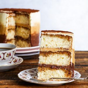 A slice of the gluten free tiramisu cake is on a decorative plate in the foreground. The layers of fluffy genoise, soaked in coffee, as well as chocolate, coffee and plain mascarpone buttercream are nicely distinguishable. The rest of the gluten free tiramisu ombre cake is in the background. Chocolate Coffee Desserts, Gluten Free Lemon Drizzle Cake, Orange Polenta Cake, Mascarpone Buttercream, The Loopy Whisk, Loopy Whisk, Gluten Free Tiramisu, Vegan Gluten Free Cake, Gluten Free Vanilla Cake