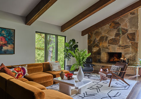 With an original stone fireplace, ceiling beams and an Eames Lounge Chair - this space embraces its Mid-Century bones while contemporary styling updates the vibe.  Design by Two Hands Interiors. View more of this home on our website. #midcentury #familyroom Mid Century Modern Stone Fireplace, Mid Century Modern Living Room Fireplace, 70s Fireplace, Midcentury Modern Fireplace, Sloped Ceiling Living Room, Living Room 70s, Modern Stone Fireplace, Mid Century Fireplace, Edge Of The Forest