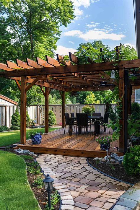 Wooden pergola on a backyard deck with outdoor dining set. Paved pathway leads to the deck, surrounded by lush greenery and decorative plants. Shade Structure Backyard, Landscaping Around Pergola, Backyard Patio Designs Small Yard, Pergola Off The House, Wood Deck With Pergola, Pergola Accessories Outdoor, Pergola And Deck, Diy Wooden Pergola, Pergola Next To House