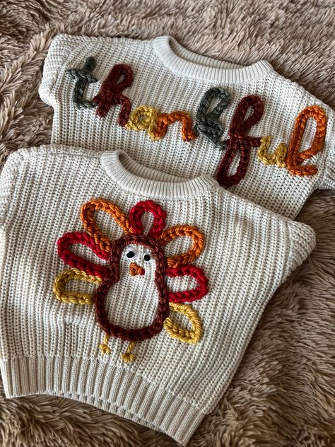 HAND-EMBROIDERED SWEATER -- This listing is for you choice of one hand-embroidered Thanksgiving sweater. This cream sweater features either a multi-colored turkey or the word "thankful" in alternating fall yarn colors. These chunky knit kids' sweaters are made with soft, breathable cotton, are great for daily wear, and look fantastic over jeans or leggings! These sweaters have a round neck and long sleeves, and are made to fit a bit oversized. Recommended care: Hand wash or wash on gentle cycle Pumpkin Embroidery Sweater, Yarn Embroidered Sweater, Fall Embroidered Sweater, Embroidered Knit Sweater, Embroidery Sweater Ideas, Yarn Embroidery On Sweater, Sweater Embroidery Ideas, Embroidered Sweater Diy, Embroidery Sweater Diy