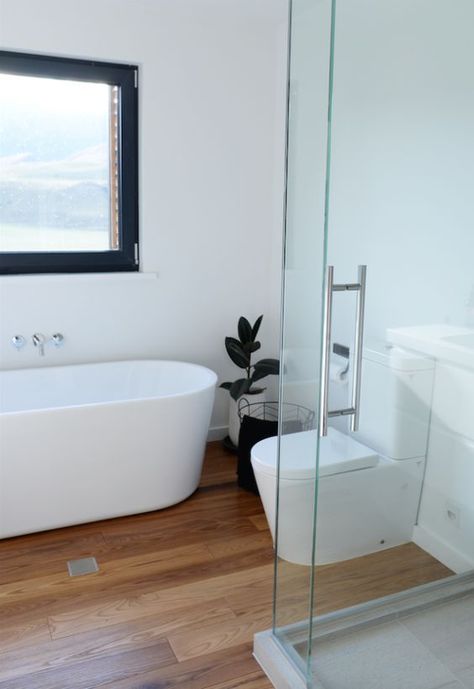 a minimalist white bathroom with a light stained wood floor, a shower space, an oval tub and some dark touches for more drama Wooden Bathroom Flooring, Bathrooms Wooden Floor, Wooden Floor Bathroom Small, Small Bathroom With Wood Floor, Wooden Floor In Bathroom, Bathroom Ideas Wooden Floor, Toilet Wooden Floor, Wooden Floor Bathroom Ideas, Wooden Flooring Bathroom