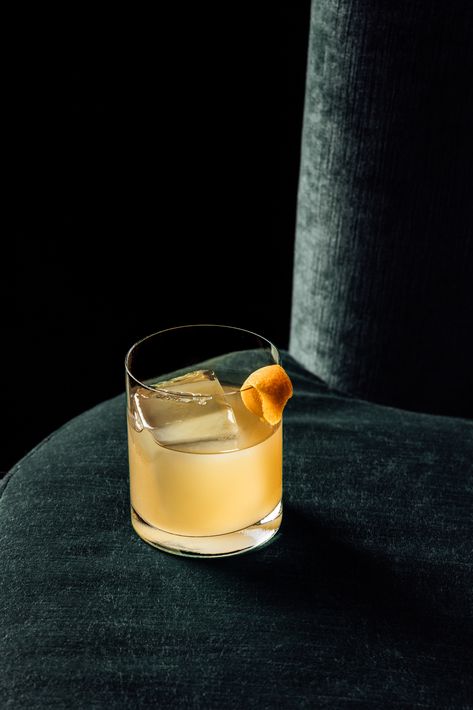 Yellow cocktail in a short clear glass with large ice cube and orange peel sitting on a green velvet sofa with black background Retro Cocktail Photography, Restaurant Cocktail Photography, Bar Photography Ideas, Cocktail Foto, Drinks Photoshoot, Cocktail Shoot, Cocktails Photography, Nobu Restaurant, Sarah King