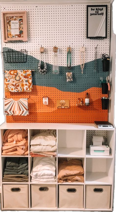 Small business packing station peg board with tee shirts Peg Board Tshirt Display, Small Business Apparel Ideas, Home Office Packing Station, Boutique Shipping Station, Local Store Aesthetic, Small Craft Shop Interior, Small Biz Aesthetic, She Shed Ideas For Small Business, Small Business Space Ideas