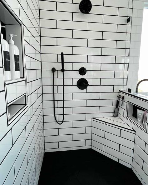 Shower bench ideas are displayed in this bathroom with a corner bench and a built-in niche. White subway tile with black grout displays a black faucet and a second niche on the opposite wall. Black flooring contrasts with the white space. Black Shower Pan Ideas, Subway Tile Shower With Niche, White Tile Black Grout, Subway Tile With Black Grout, Black Bathroom Floor Tiles, White Tiles Black Grout, Tile With Black Grout, Shower Bench Ideas, Shower Niche Ideas