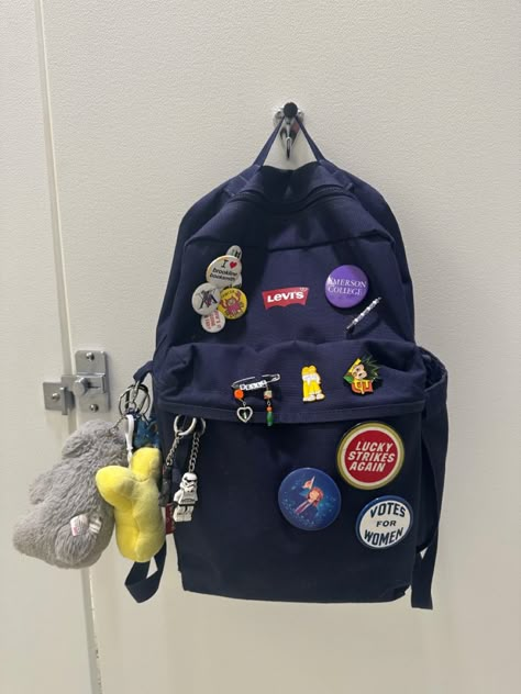 Navy blue backpack with various pins and keychains Keychains On Backpack, Backpack With Pins Aesthetic, Backpack Customize Ideas, Backpack Accessories Keychain, Levis Backpack, School Bag Keychain, Grey Jansport Backpack, Decorated Backpack, Y2k Backpack